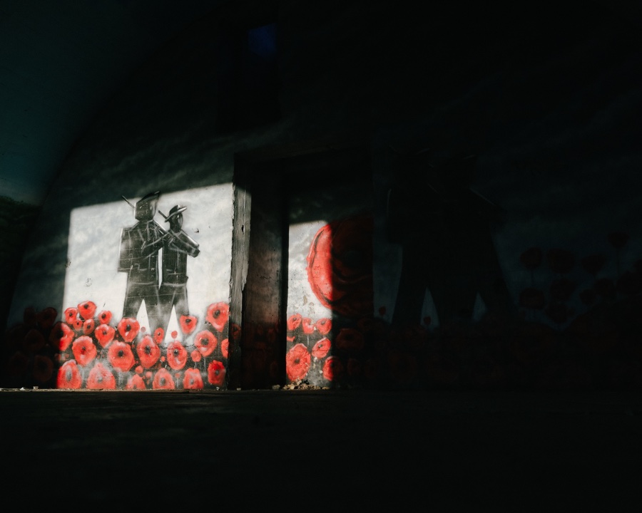 Sunlight on a mural of two soldiers and red poppies inside the dark bunker