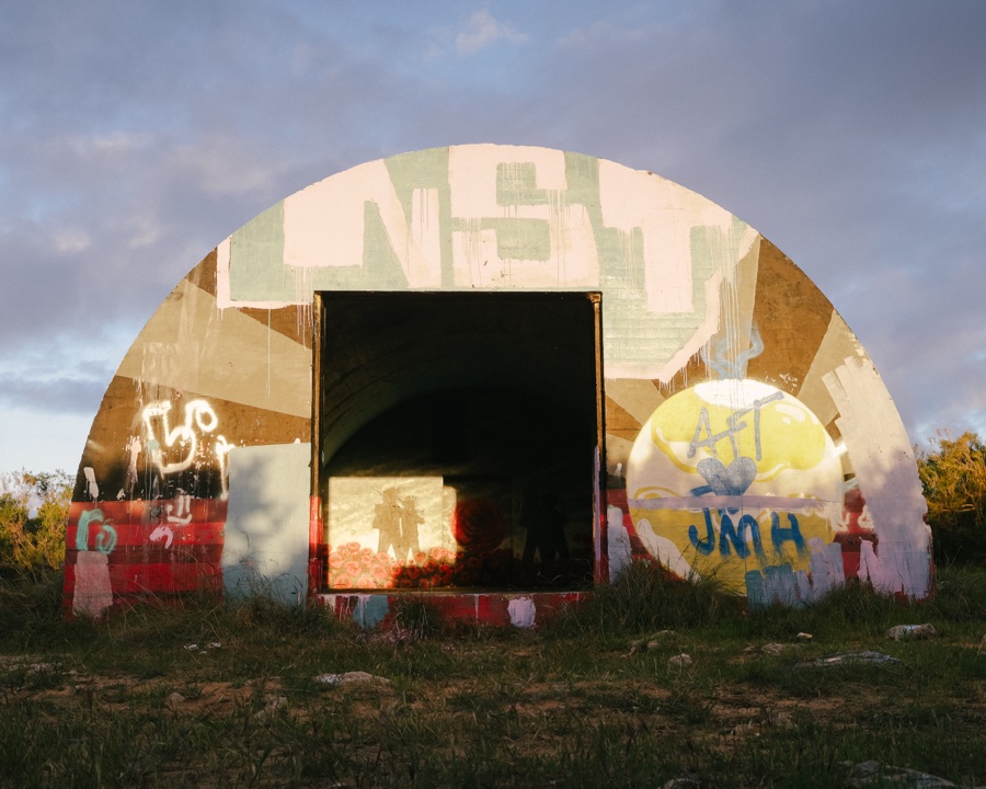 Straight-on view of the painted curved bunker façade, with a dark doorway framing a poppy mural